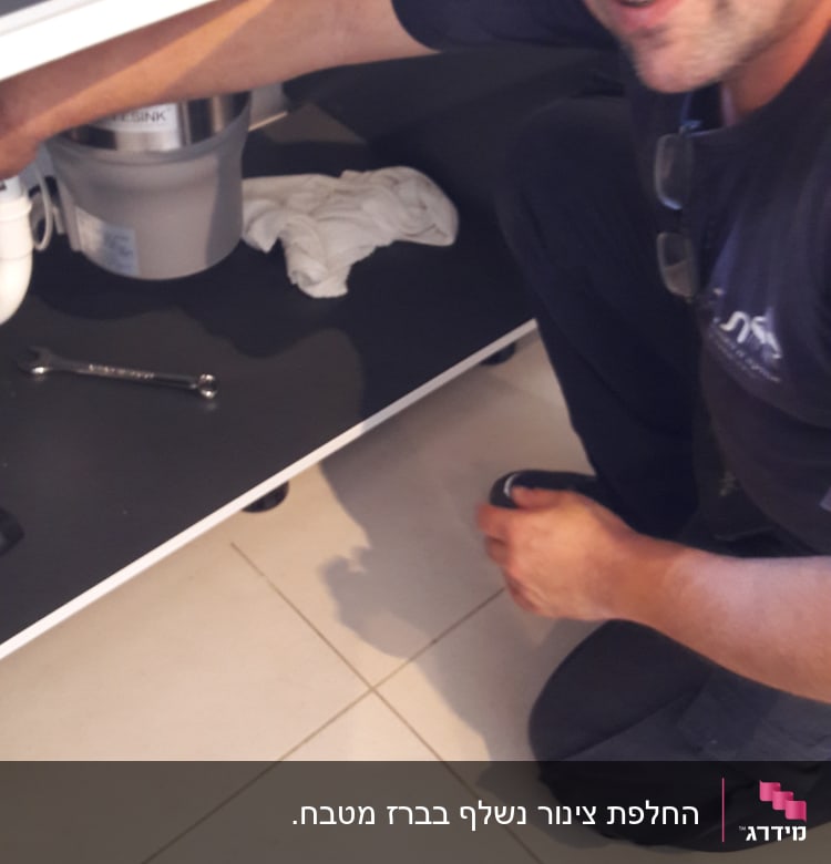 אדם מתקן צנרת מתחת לכיור עם מפתח ברגים